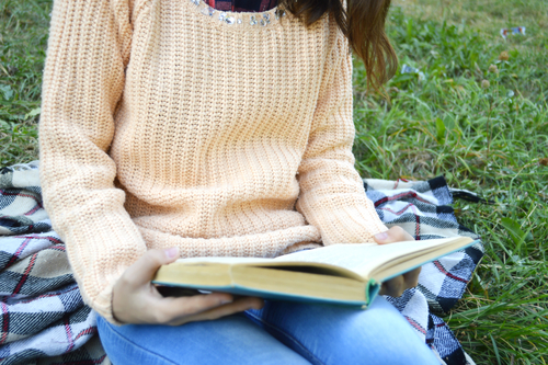 girl wearing sweater outside and reading a book